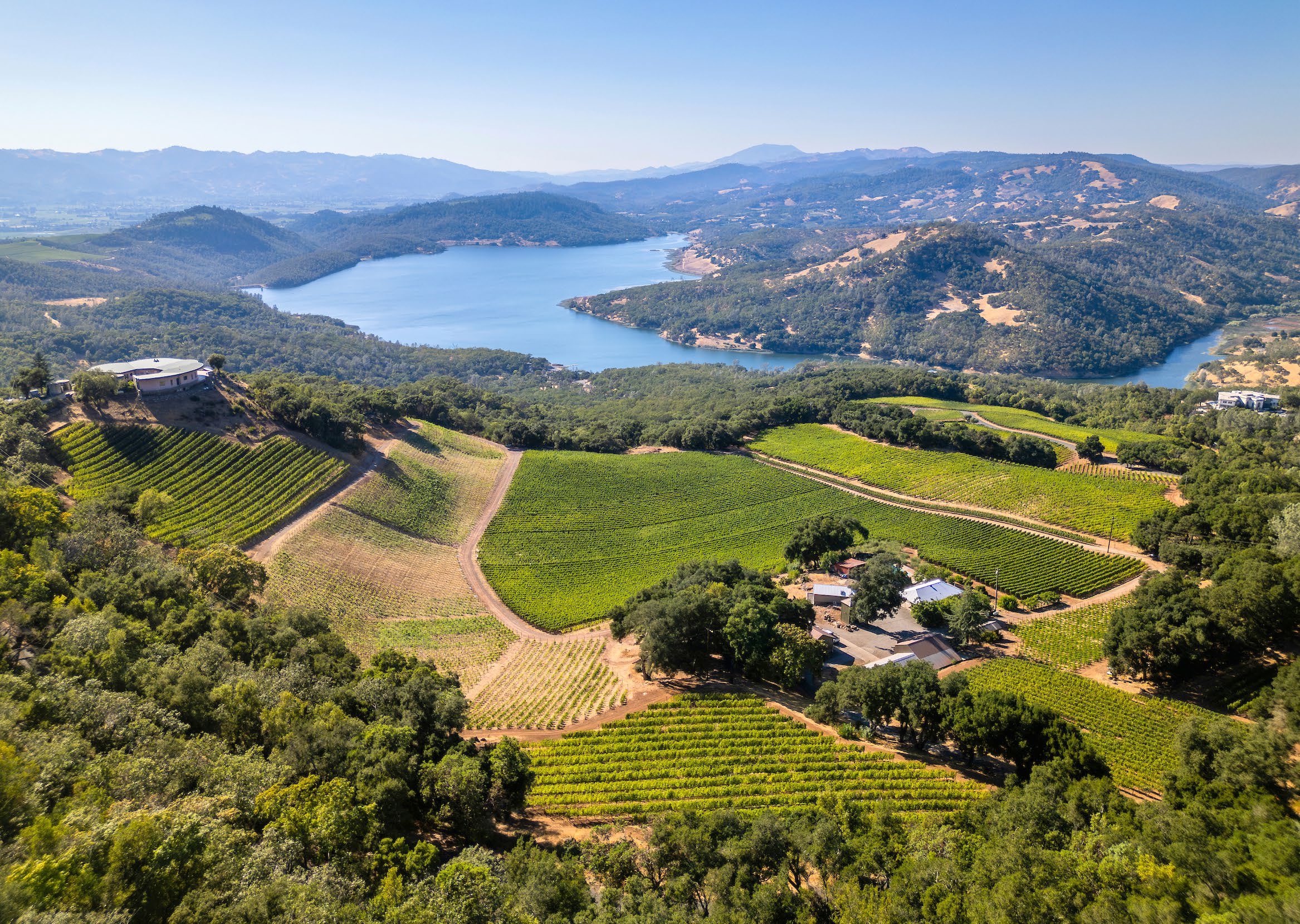 Aerial view of a hillside winery estate with vineyard blocks above a lake on Pritchard Hill in St. Helena, California