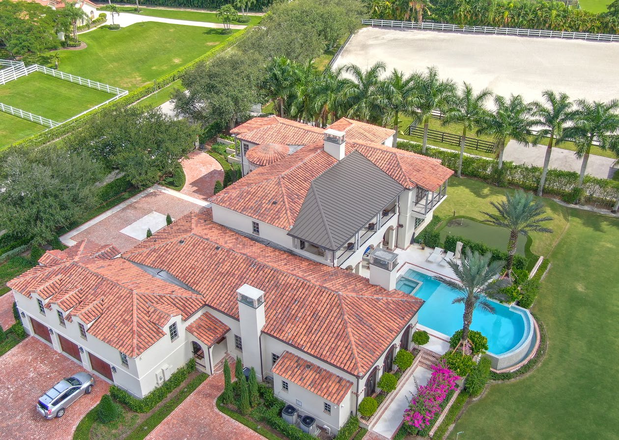Aerial view of a Mediterranean-style equestrian compound with tile roofs, pool, and riding arena in Wellington, Florida